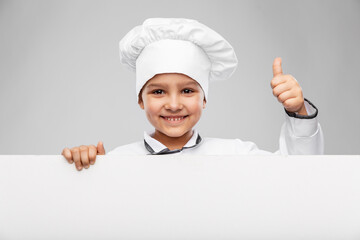 cooking, culinary and profession concept - happy smiling little girl in chef's toque and jacket with white board showing thumbs up gesture over grey background