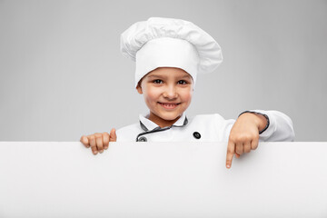 cooking, culinary and profession concept - happy smiling little girl in chef's toque and jacket pointing finger to white board over grey background