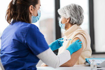 medicine, health and vaccination concept - doctor or nurse with syringe making vaccine or drug injection to senior woman in mask at hospital