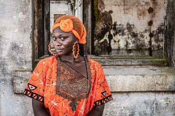 Africa Woman in orange suit and headdress stands by an old building in Takoradi Ghana West Africa - obrazy, fototapety, plakaty