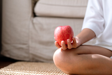 Closeup image of a young woman holding and eating a red apple at home