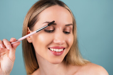 Close up beauty portrait of a woman with perfect skin and natural makeup, full nude lips, holding an eyebrow brush.