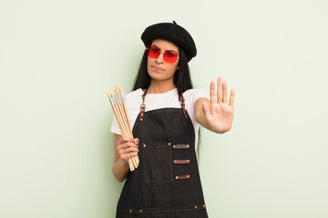 young pretty hispanic woman looking serious showing open palm making stop gesture. art student...