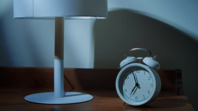 Sleepy man wakes up from a classic alarm clock close-up. Man overslept the alarm. alarm clock rings a bell standing on the bedside table, a man's hand turns off the alarm. 