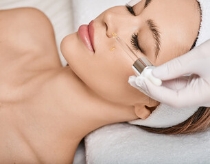 Female patient with closed eyes enjoying cosmetology procedures using treatments oils and serum to...