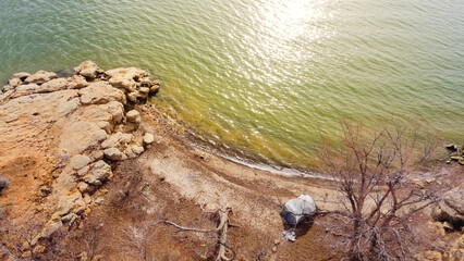 Aerial view rocky shoreline, sandstone cliff with dormant trees and large family tent at Grapevine Lake, Texas, USA