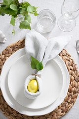 Easter elegant table setting with yellow egg, fresh greens on grey linen tablecloth. View from above. Christian religion tradition.