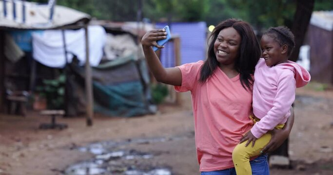 Black African Lesbian woman holding her cute daughter taking a selfie in an informal settlement slum