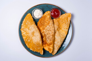 three chebureks are a culinary product in the form of a semicircle of unleavened dough with a filling of chopped fatty lamb, onions, spices. on a white background