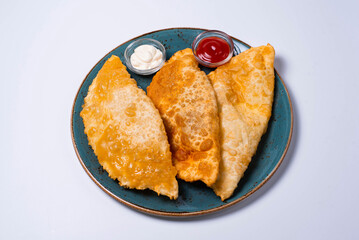 three chebureks are a culinary product in the form of a semicircle of unleavened dough with a filling of chopped fatty lamb, onions, spices. on a white background