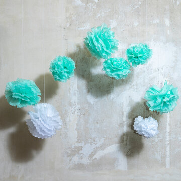 PonPons aus Papier in Mint und wei&szlig; vor einer Wand mit abgekrazter Tapete