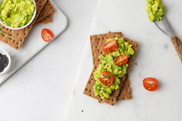 Top view of toast with avocado paste on bread with tomatoes cherry and arugula on white table. Breakfast