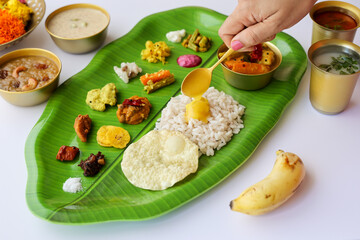Woman hand serving parippu dal curry ghee traditional Onam sadhya rice Sambar, Rasam, Pappadom Payasam on banana leaf Onam Vishu Pongal Diwali festival vegetarian food Kerala Tamil Nadu South India.