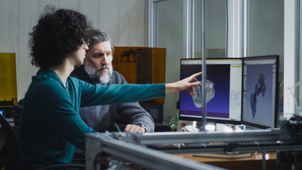 Young man pointing at computer monitor and discussing 3D models with mature customers while sitting...