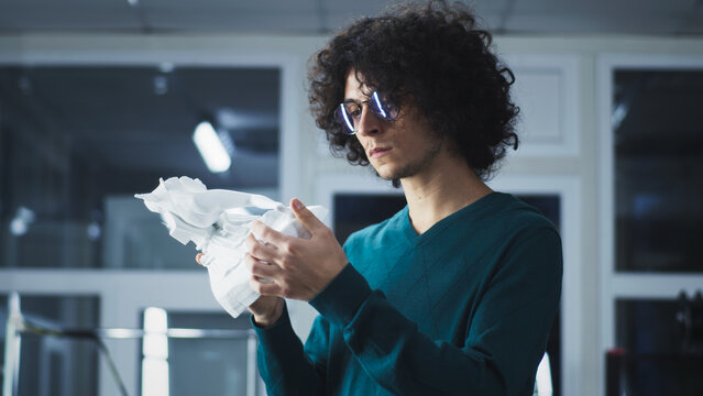 Man in casual clothes with curly hair examining plastic statuette from 3D printer while working in workshop of modern design studio