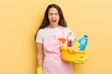 young pretty hispanic woman shouting aggressively, looking very angry. housework an clean products...