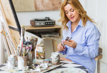 Mature woman painting brush on canvas at home.