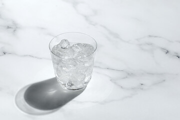 Cold water in glass with ice on sunny marble background, dark shadow. Creative concept