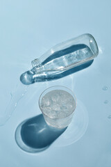 Lying bottle of water ang glass of water with ice on sunny blue background. Dark shadow