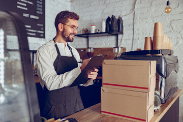 Cheerful male barista writing on clipboard in cafe