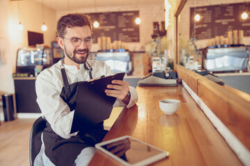 Joyful male barista writing on clipboard in cafe