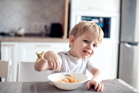 cute little child with appetite eats himself at home in the kitchen. The boy smiles, looks into the camera. Healthy food, natural vitamins, baby dieting concept. selective focus