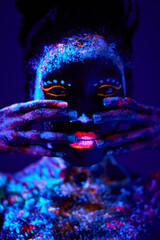 beautiful young black female with fluorescent prints on face, unusual prints, body art, posing at camera. neon lights, uv ray, luminescence concept. model touching face, covering. close-up portrait