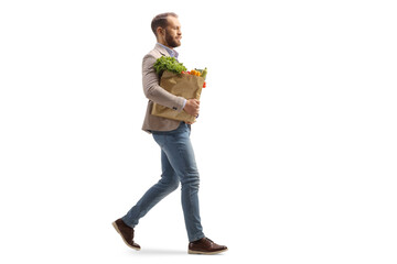 Full length profile shot of a young man carrying a grocery bag and walking