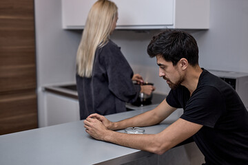 Unhappy young caucasian woman and bearded man not talking after quarrel, in kitchen, frustrated blonde wife and husband ignoring each other, relationship problem, family crisis concept