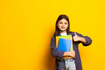 Cute little girl with books on yellow background.