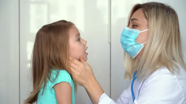 Female doctor pediatrician examining little girl patient in clinic. Doctor checks childs throat. Medicine and healthcare concept.