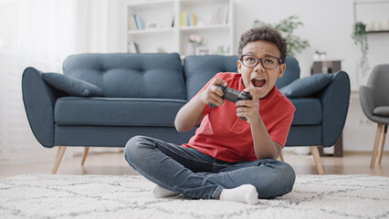 Excited African American boy playing video game with joystick controller at home