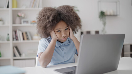 Portrait of little girl sitting in front of laptop, tired of exhaustive studying