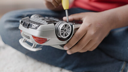 African American boy fixing broken toy car with screwdriver, learning new skills
