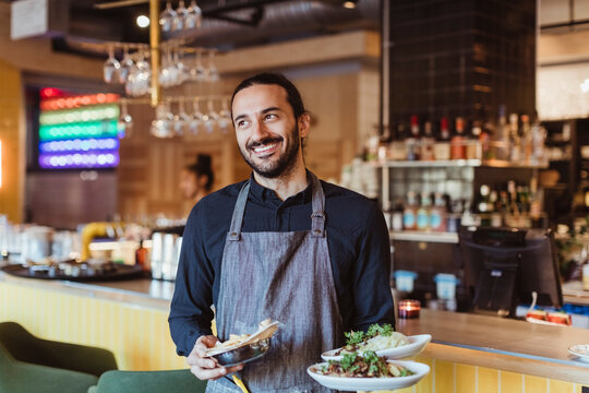 Happy male waiter with food looking away in bar