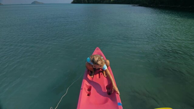 Pretty slim woman in elegant swimsuit lies in pink plastic kayak drifting on azure ocean at exotic resort upper view.