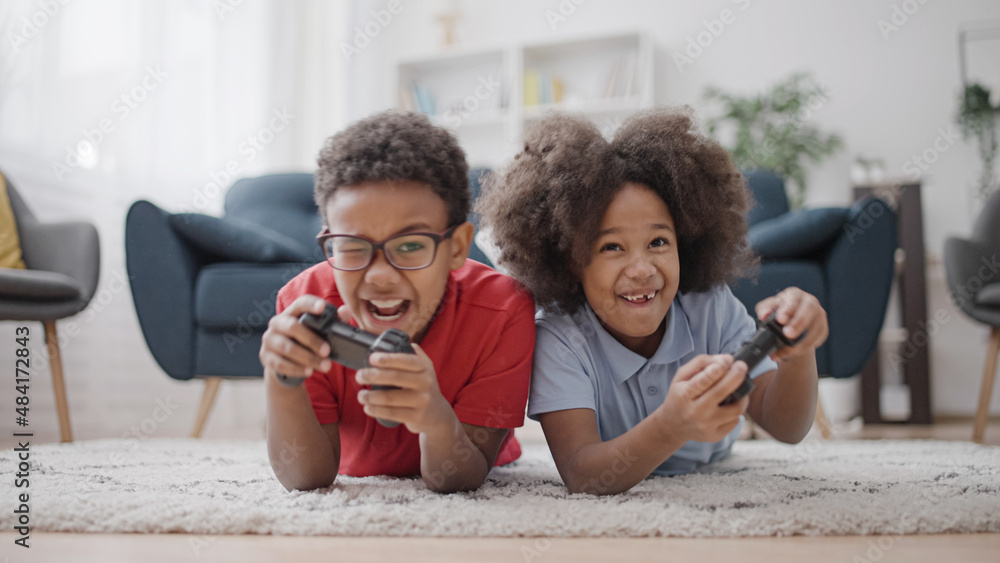 Wall mural Two active african american kids playing video game on floor having fun together