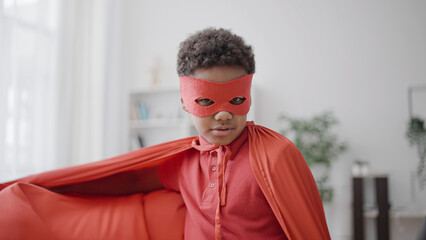 African american little boy wearing superhero costume, playing game at home