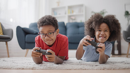 Excited black siblings holding joysticks, playing video games, competing with each other