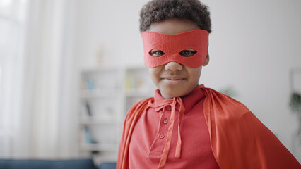 African american boy in red cloak and mask looking at camera, pretending to be superhero