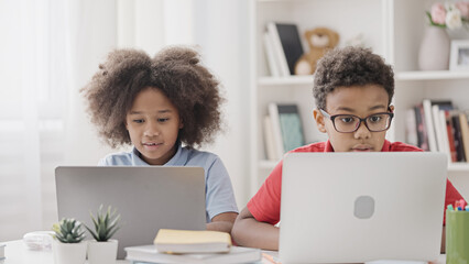 Two curious kids studying together on laptops enjoying learning process, smiling