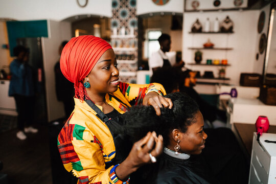 Female barber making hairstyle of customer in hair salon