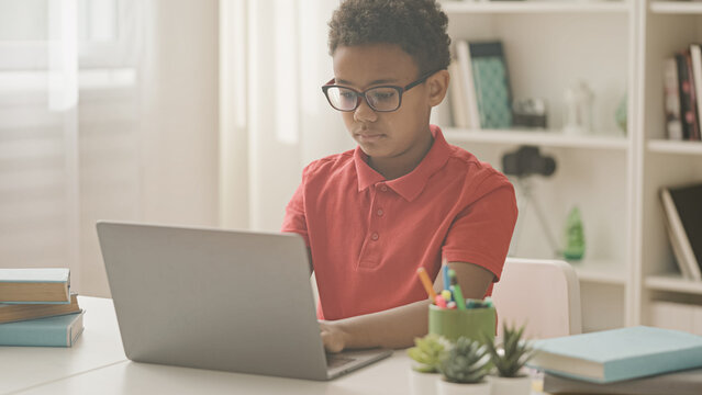 African american boy in eyeglasses studying online on laptop at home, difficulties