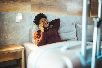 Confident businesswoman in casual wear having a phone call and smiling in a hotel room. Next to her is a black suitcase as she prepares to check out of the hotel. End of a business trip