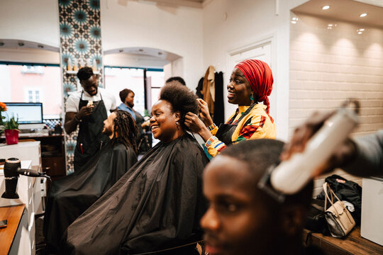 Multiracial hair expertise making hairstyle of male and female customers at barber shop