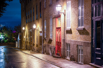 Fototapeta na wymiar A Red Door To A Residential Building Is Predominately Visible In This Night Time Photograph Of A Road In Vieux Quebec, A UNESCO World Heritage Site. 