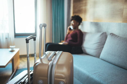 Close-up of luggage and blurred background of a happy tourist woman in a hotel after check-in. The concept of travel and vacation. She reports that she arrived safely via her smartphone