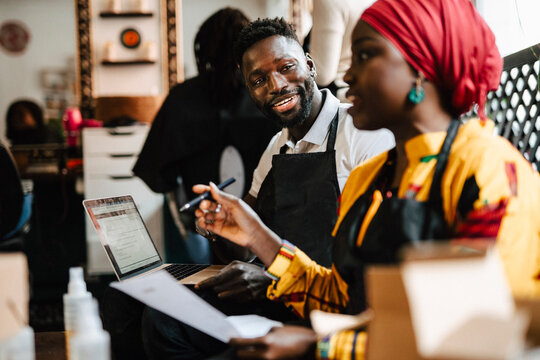 Smiling male hairdresser discussing with female coworker in barber shop