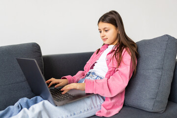 Little girl surfs on the internet sitting on the sofa.