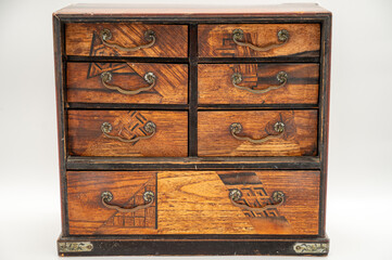 An Antique Jewelry Box Sits Facing Us Directly In Frame With Little Ornate Drawers Closed Holding Treasures Inside.